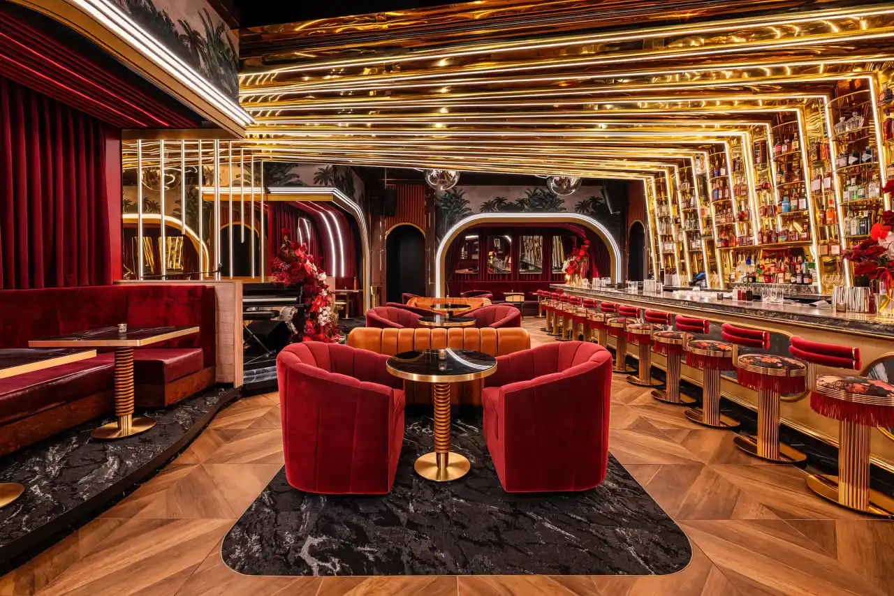 The lounge at Tell Your Friends: red velvet chairs under gold arches