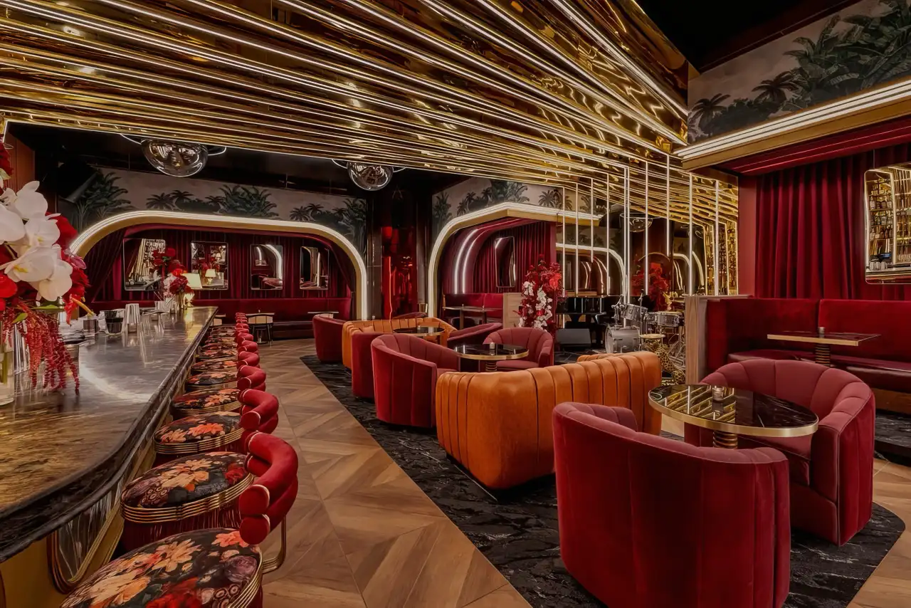The lounge at Tell Your Friends with red velvet chairs under gold light